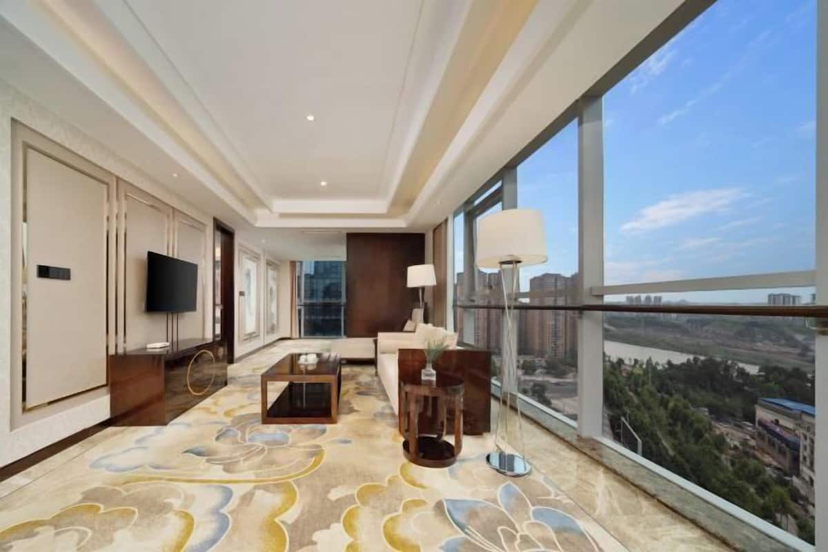 A hotel room with a large window, a flat-screen TV, a sofa, a coffee table, and a decorative rug.