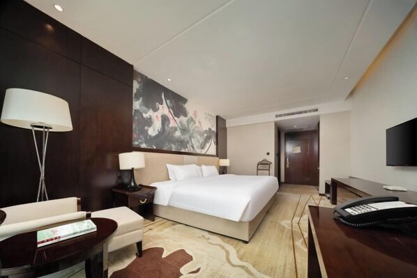 A hotel room with a large bed, a desk with a telephone, a chair, a lamp, and a painting on the wall. - Neijiang International Hotel (Wanda E-commerce Center) (Neijiang)