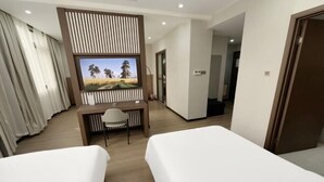 Een hotelkamer met twee bedden, een bureau met stoel, een aan de muur bevestigde televisie en een deur aan de rechterkant.