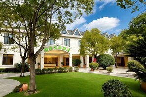 Un hôtel doté d’une entrée abritée, d’une pelouse bien entretenue et d’une variété d’arbres et d’arbustes.