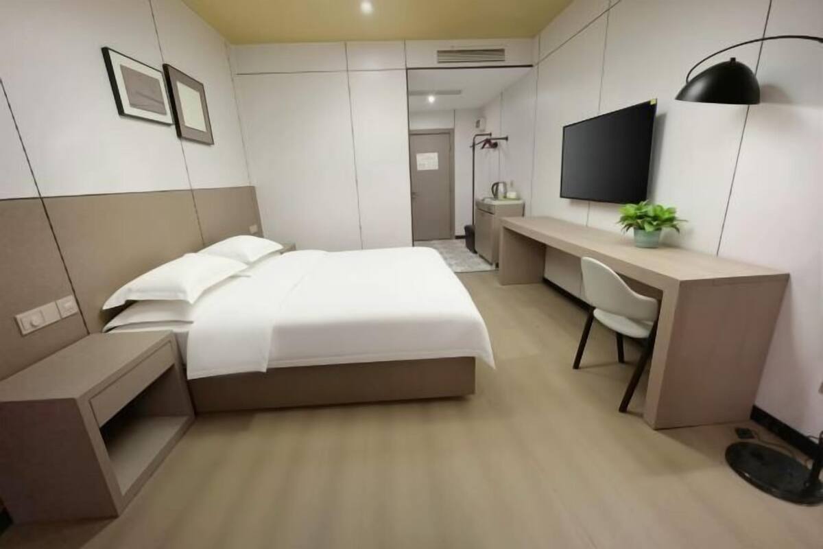Ein modernes Hotelzimmer mit Bett, Schreibtisch, Stuhl, Fernseher und einer kleinen Pflanze.