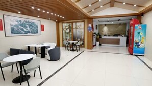 Een hotel lobby met een receptiebalie, een zithoek met tafels en stoelen, en een automaat.