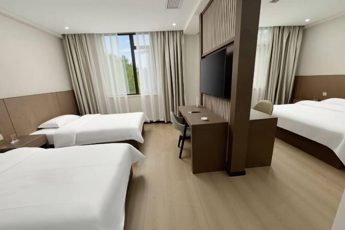 Ein Hotelzimmer mit zwei Betten, einem Schreibtisch, einem Fernseher und großen Fenstern mit Vorhängen.