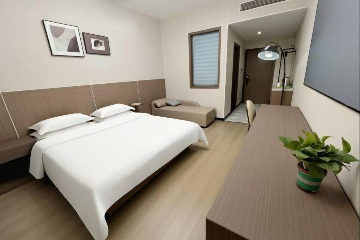 Ein Hotelzimmer mit Bett, einer kleinen Sitzecke, einem Schreibtisch, einer Lampe und einer Pflanze.
