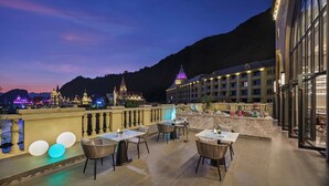 A rooftop terrace with outdoor seating, a pool, and a view of a mountain and lit-up buildings in the background. - Yingde Chocolate Kingdom Hotel (Qingyuan)