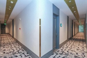 Un pasillo de hotel con alfombra estampada, una puerta azul y señalización direccional.