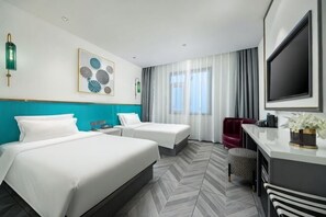 Habitación de hotel con dos camas, un escritorio, un televisor y un ventanal grande con cortinas.