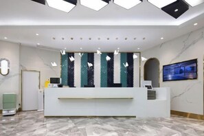 Un área de recepción con un mostrador blanco, pared con diseño, televisor y piso de mármol.