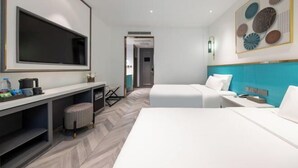 Habitación de hotel con una amplia televisión de pantalla plana, un escritorio con una silla, dos camas y una obra de arte colgada en la pared.