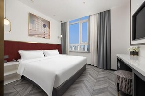 Ein Hotelzimmer mit Bett, Schreibtisch, Fernseher, einem Fenster mit Vorhängen und Blick auf die Stadt.