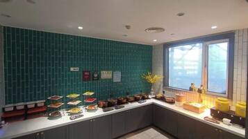 Una cocina moderna con salpicadero verde azulado, una encimera larga con diversos alimentos y un ventanal que proporciona luz natural.