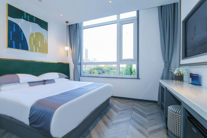 A hotel room with a bed, a desk, a television, a window with curtains, and a painting on the wall.