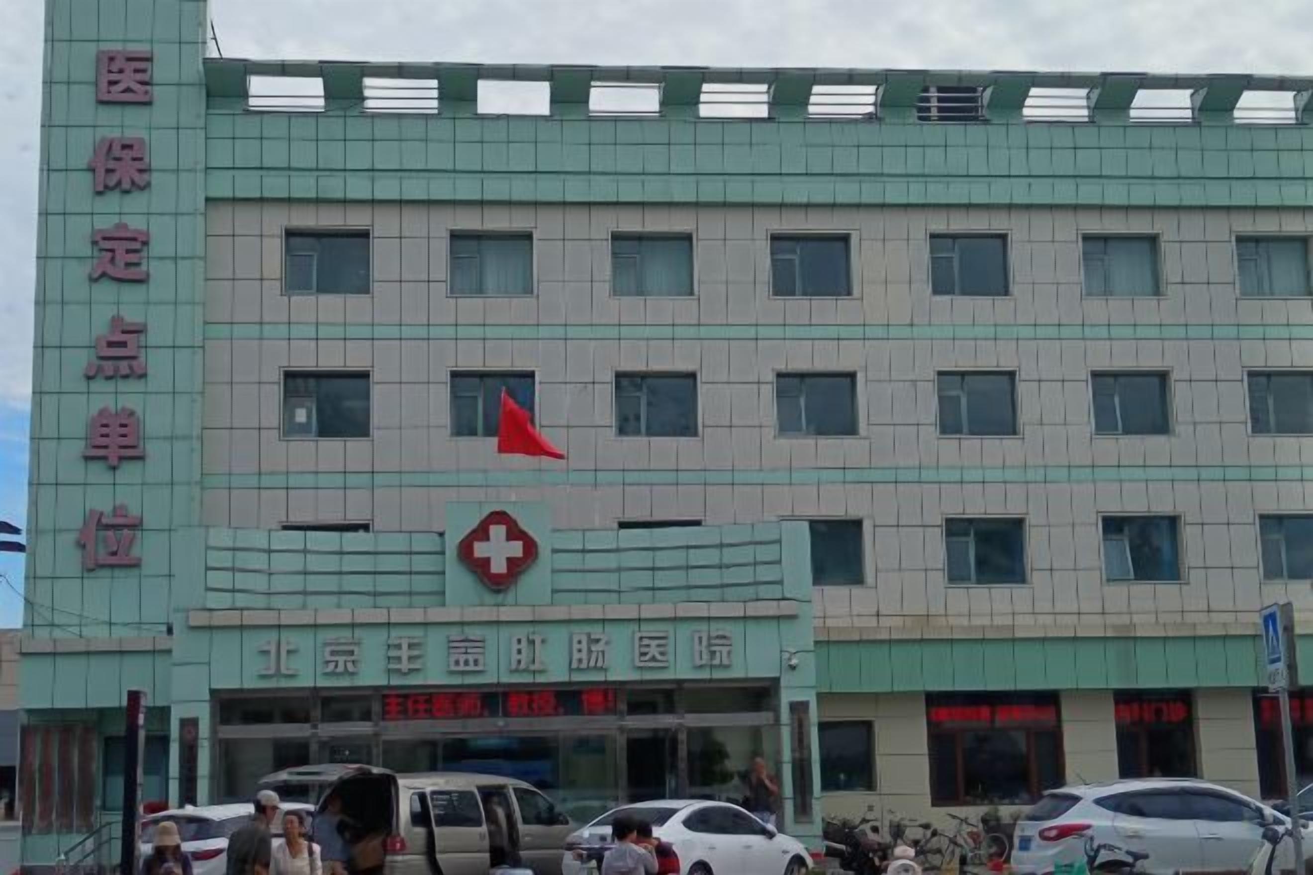 Um edifício com vários andares e um grande símbolo de cruz vermelha, indicando que se trata de uma unidade médica. Várias janelas na fachada e sinalização no térreo para diferentes departamentos ou serviços.