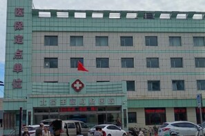 Un edificio de varios pisos con un llamativo símbolo de la cruz roja, que indica que se trata de una instalación médica. Cuenta con varias ventanas en la fachada y letreros en la planta baja que identifican diferentes departamentos o servicios.