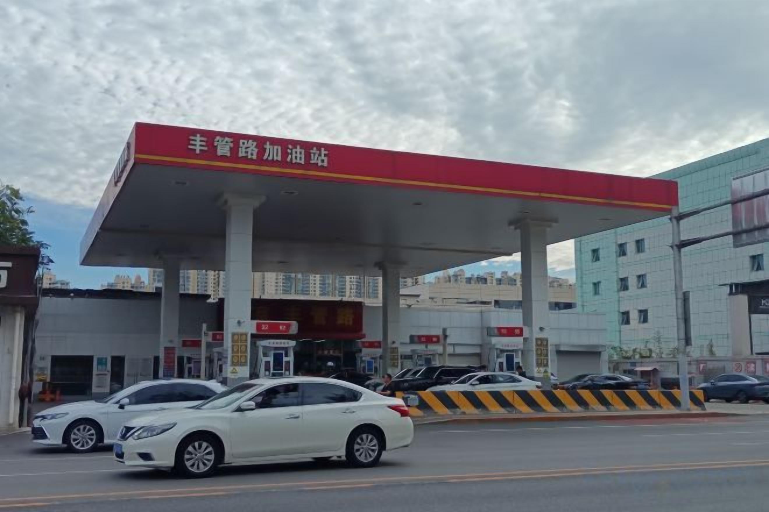 Um posto de combustível com várias bombas de abastecimento, uma cobertura vermelha e alguns carros estacionados em frente.