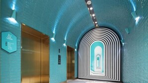 Un pasillo interior con pared de azulejos azules, un ascensor dorado y un arco decorado.