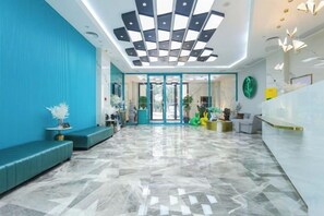 Un hall de hotel con mostrador de recepción, zona de estar y piso estampado.