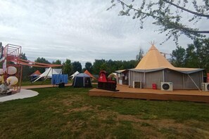 A campsite with tents, a play structure, and a small building with a red mailbox.