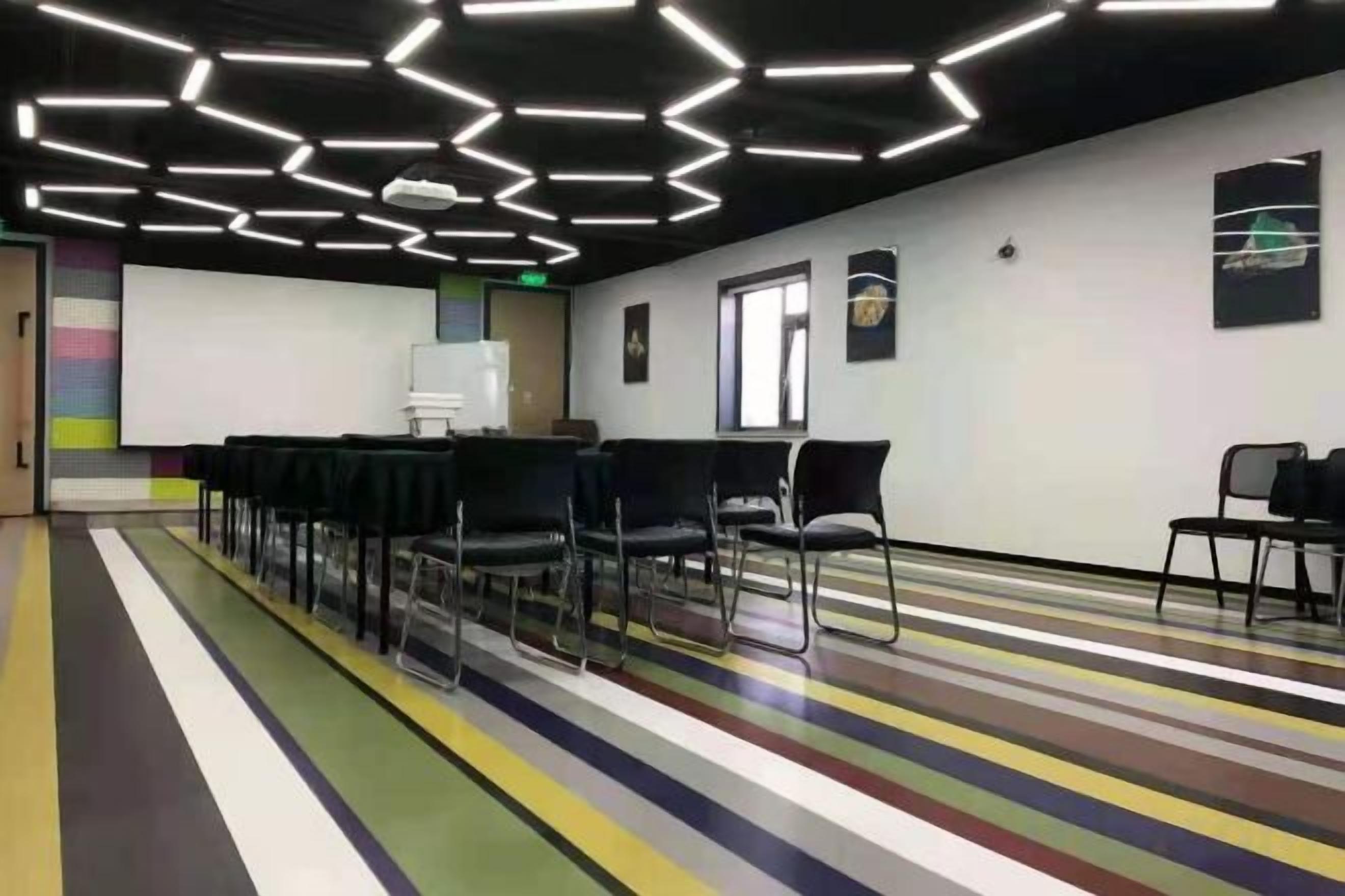 Un salón de conferencias con una pantalla de proyector, sillas y una alfombra a rayas coloridas.