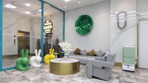 Un vestíbulo moderno con área de descanso, un elemento decorativo de color verde en la pared y una recepción.