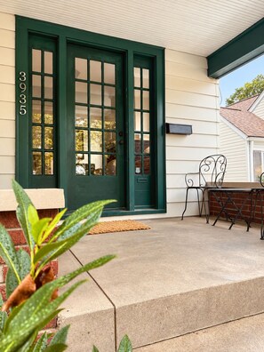 Une maison avec une porte d’entrée verte, une boîte aux lettres et un petit espace extérieur aménagé avec une table et des chaises.