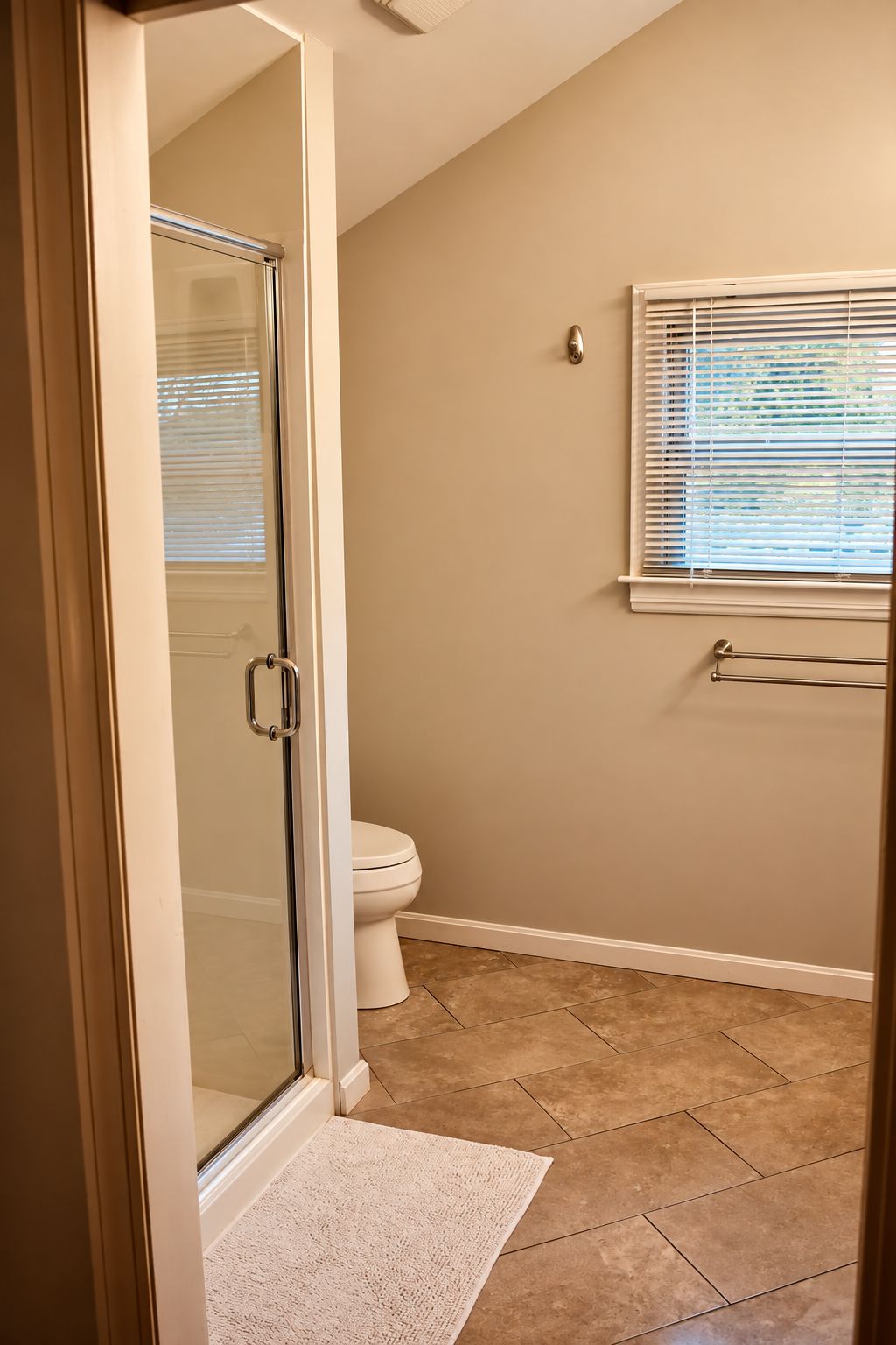 Een badkamer met een douchecabine van glas, een toilet en een raam met zonwering.
