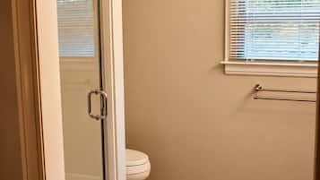 Een badkamer met een douchecabine van glas, een toilet en een raam met zonwering.