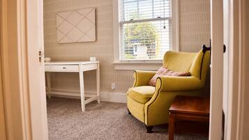 Una habitación con un sillón amarillo, un escritorio blanco y una ventana con persianas.