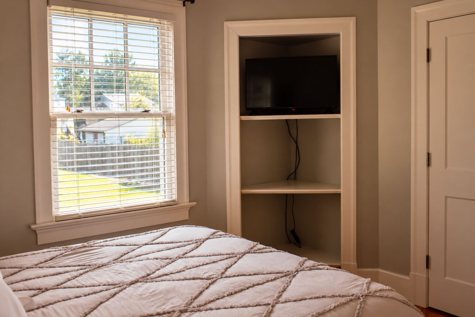 Quarto com cama, janela com persianas, televisão em uma estante e porta.