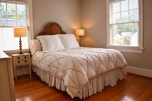 A bedroom with a wooden headboard, a bed with a quilted bedspread, two bedside lamps, a nightstand with drawers, and a window with blinds. - St. Matthew’s - Walk to Shops & Restaurants (Louisville)