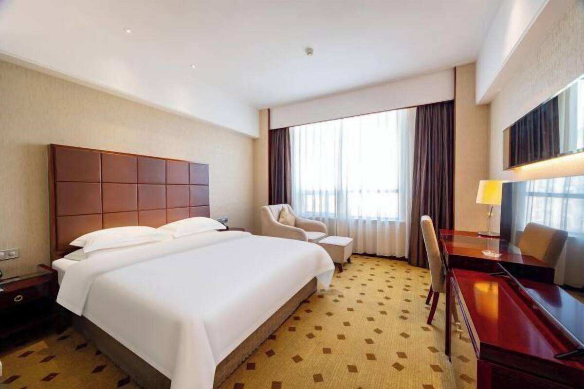 Een hotelkamer met een groot bed, een bureau, een stoel en een raam met gordijnen.
