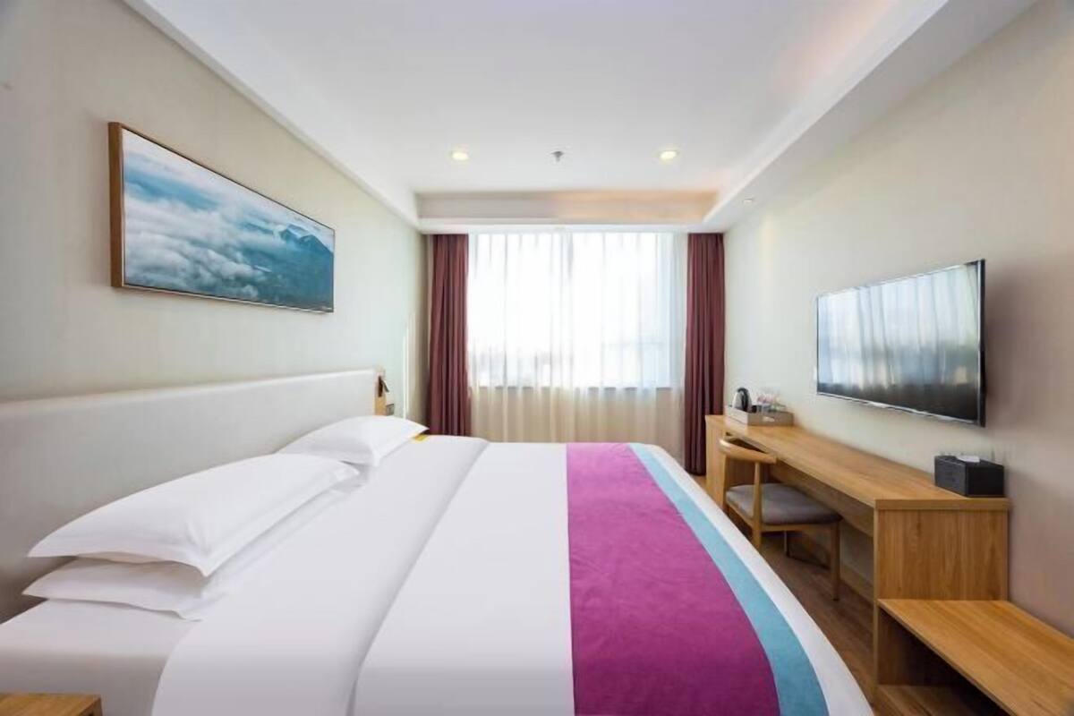 Een hotelkamer met een bed, een bureau, een televisietoestel en een raam met gordijnen.