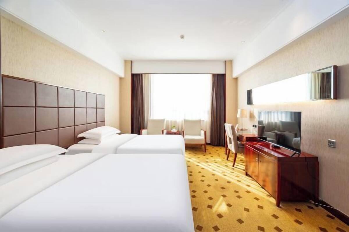 Een hotelkamer met twee bedden, een bureau, een stoel, een televisie en een groot raam.