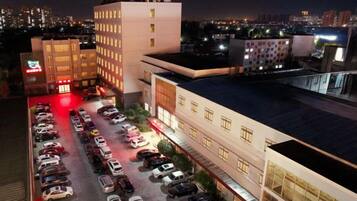 A multi-story hotel with a parking lot filled with cars, a large illuminated sign, and a cityscape in the background.