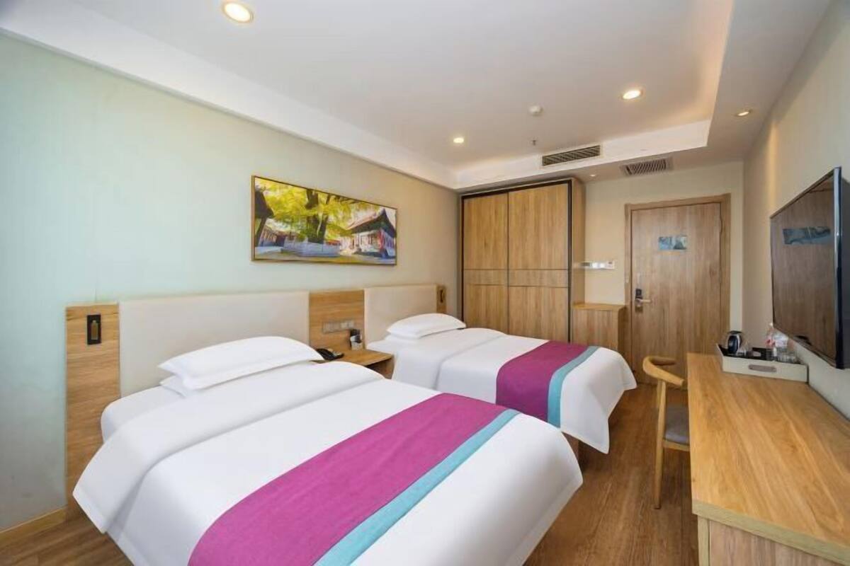 Een hotelkamer met twee bedden, een houten bureau, een televisie en een schilderij aan de muur.