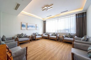 A spacious living room with a wooden floor, multiple sofas, and a large window with curtains. - Yuanzhongfang Hotel (Pingdu)