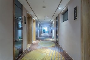 Un largo y estrecho pasillo de hotel con alfombra estampada, puertas a ambos lados y cuadros en las paredes.
