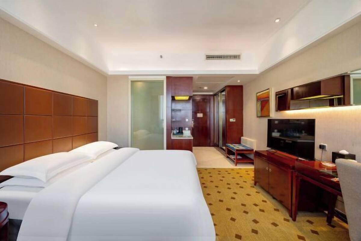 Een hotelkamer met een groot bed, een bureau met stoel, een televisie en een kledingkast.