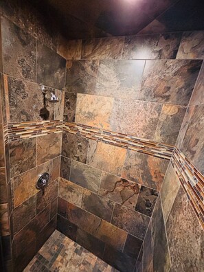 A shower with stone tiles and a metal showerhead.