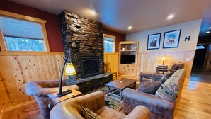 A cozy living room with a stone fireplace, leather sofas, a wooden coffee table, and a television. - Lakefront Home on the Whitefish Chain - Outdoor Pool, Pickleball Courts and More (Pequot Lakes)