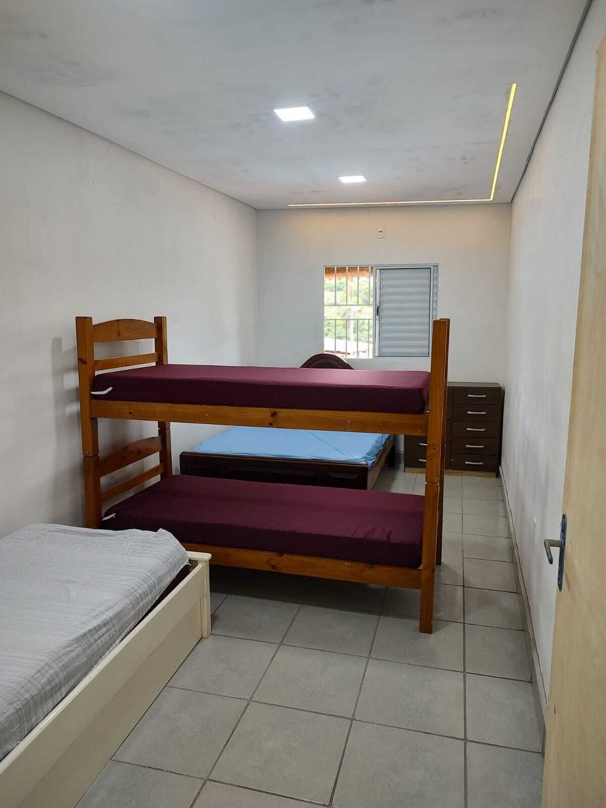 Una habitación pequeña y estrecha con literas, una ventana con persianas y un escritorio con cajones.