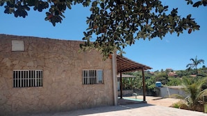 A stone building with two barred windows, a covered patio, and a view of a hilly landscape. - Rancho Dos Anjos Farm in Campinas - Daily Rates, Seasons and Events (Campinas)