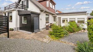 A two-story house with a black garage door, a small patio with chairs, and a gravel driveway. - Beautiful home in Aabenraa with WiFi (Aabenraa)