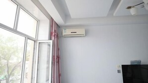 Une chambre dotée d’une grande fenêtre, d’un climatiseur, d’un téléviseur à écran plat et d’un ventilateur de plafond.