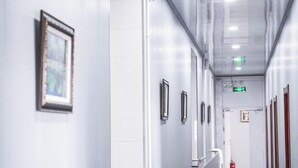 A corridor with white walls, framed pictures, and a fire extinguisher. - Huma Hongyue Hotel (Huma)