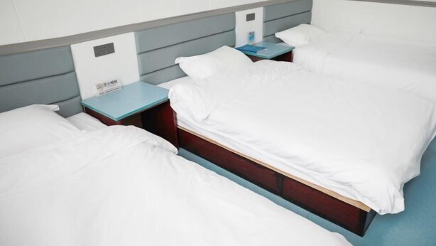 Une chambre d’hôtel avec deux lits simples, une table de chevet avec un téléphone et une petite table avec un livre.