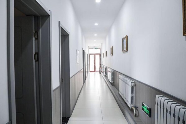 A long, narrow hallway with doors on both sides, a radiator on the right, and a sign with a green arrow.