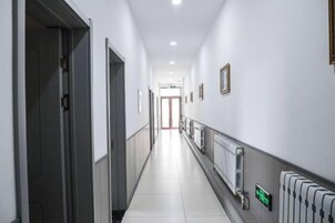 Un pasillo largo y estrecho con puertas a ambos lados, un radiador a la derecha y un letrero con una flecha verde.