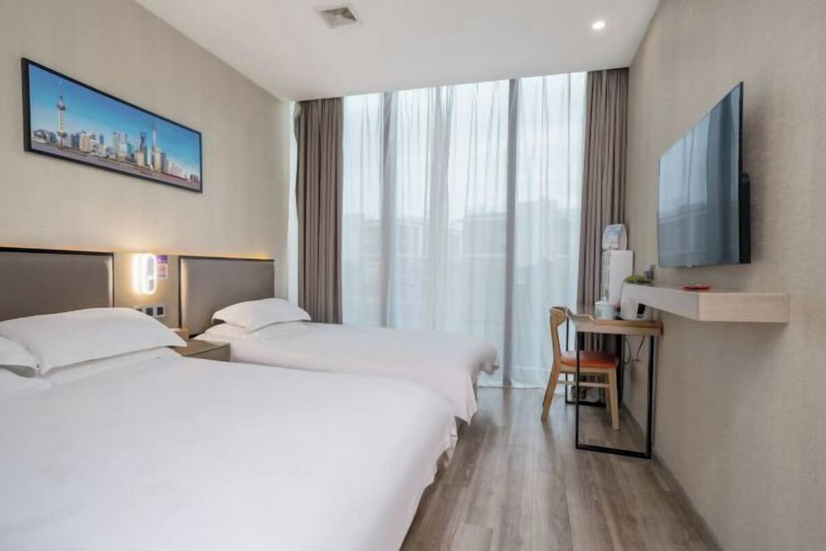 Hotelkamer met twee bedden, een bureau met stoel, een televisie en een stadsgezichtschilderij.