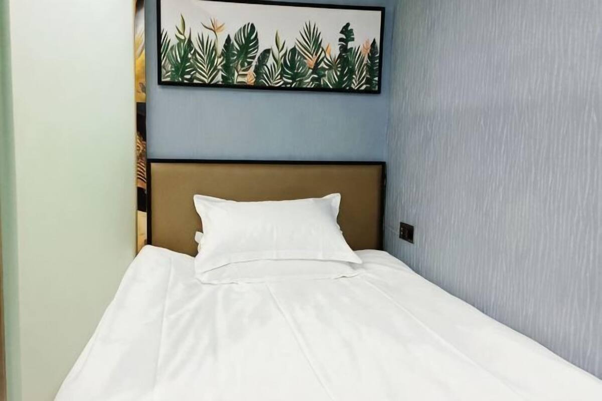 Een opgemaakt bed met witte lakens, een bruin hoofdbord en een schilderij met een tropisch thema aan de muur.
